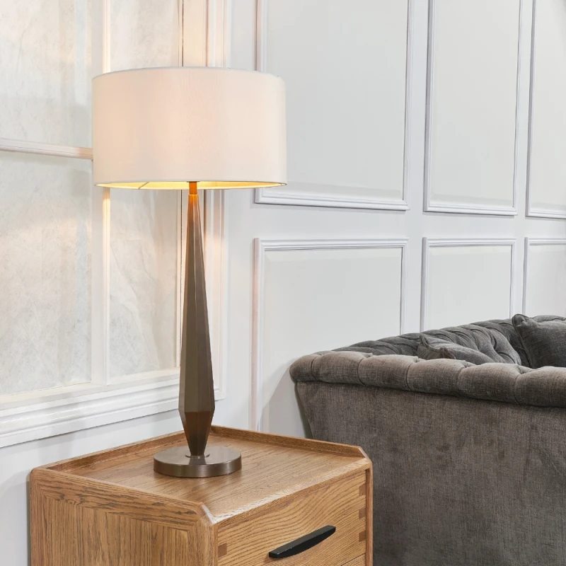 Lampa stołowa Belrose Brass z kremowym abażurem ustawiona obok sofy